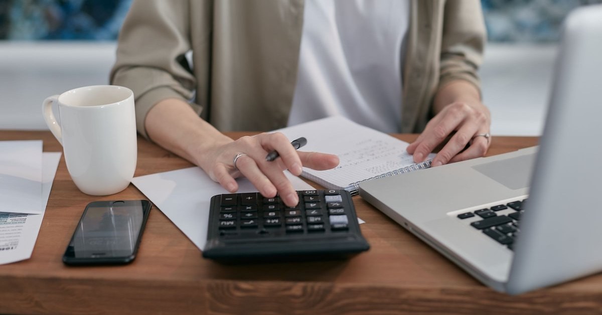 Person using a calculator and laptop to budget for the subsequent temporary application charge